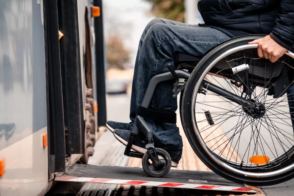 Close-up of person in wheelchair wearing jeans entering public bus on ramp.